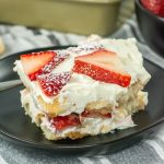 A delectable slice of No Bake Strawberry Tiramisu delights with its creamy layers and delicate sponge, elegantly presented on a sleek black plate.
